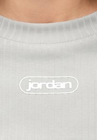 Κοντινό πλάνο από γκρι ριγέ ύφασμα πουκάμισου με λευκό λογότυπο "jordan" κεντραρισμένο στην περιοχή του στήθους.