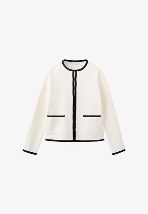 Cárdigan blanco con ribete negro, cuello redondo y cierre frontal con botones. Cuenta con dos bolsillos delanteros y mangas largas. Textura de tela suave.