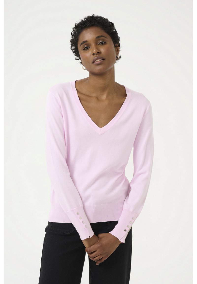 Maglione rosa a V con maniche lunghe, dotato di dettagli a bottoni sui polsini, realizzato in un materiale morbido e leggero. Pantaloni neri visibili.