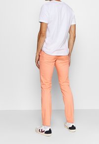 Pantaloni in cotone leggeri di colore pesca pastello con una vestibilità slim. Abbinati a una t-shirt bianca a girocollo semplice e sneakers bianche con dettagli colorati.