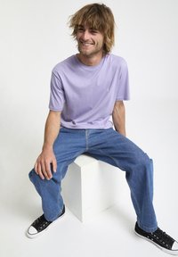Kortærmet lavendel t-shirt med rund hals, parret med lyseblå denim jeans og sorte sneakers med hvide såler.