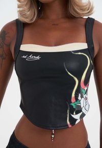 Top corto negro con un acabado brillante, con un diseño floral y acentos dorados. Banda crema en la parte superior con costura decorativa. Charm decorativo en el dobladillo.