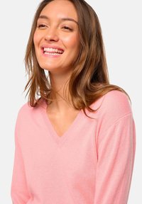 Un pull rose en V fabriqué dans un tissu doux, avec des manches longues et une coupe décontractée. Texture lisse avec des détails de couture subtils.