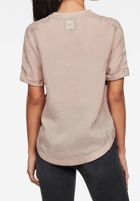 Camicia a maniche corte color rosa pallido realizzata in tessuto morbido, con risvolti sulle maniche, orlo curvo e un piccolo etichetta sul retro del collo.