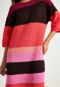 Strikket sweaterkjole med brede horisontale striber i nuancer af pink, rød og mørkebrun, med en afslappet pasform og ærmer til albuerne.