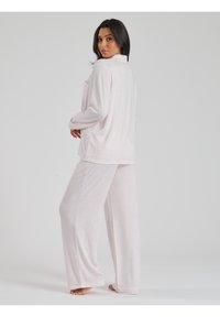 Set di pigiama rosa chiaro realizzato in morbido tessuto a costine. Caratterizzato da maniche lunghe, una tasca sulla maglietta e pantaloni larghi e dai tagli ampi.