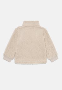 Pull en polaire couleur crème avec un col haut, surface texturée, manches longues et ourlets côtelés. Apparence douce, chaude et confortable.