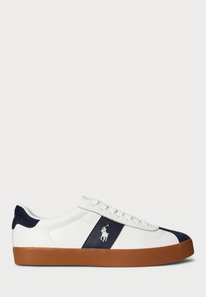 Zapatilla blanca de cuero con franja azul marino y logo, suela de goma marrón, cordones blancos y lengüeta negra en el talón.