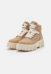 Bottes chelsea en daim couleur tan avec une semelle épaisse et texturée crème et des lacets beige. Caractéristiques œillets en métal et col rembourré.