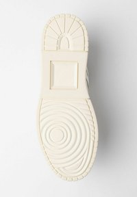 Sola della scarpa in crema chiaro con modelli di grip testurizzati; presenta forme circolari e rettangolari, accenti in rilievo e una finitura liscia.