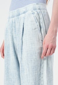 Heledad sinine, klanitud lina püksid tekstuurse pinna ja elastse vöökohaga, küljetaskutega ja vabalt istuva lõikega.