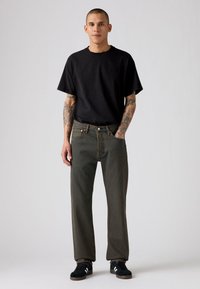 Zwarte katoenen t-shirt, losvallend. Olijfgroene denim jeans met een hoge taille, rechte pijpen en contrasterende stiksels. Zwarte sneakers met witte accenten.