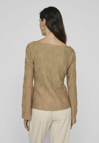 Maglia a maniche lunghe beige con un motivo testurizzato e a coste, caratterizzata da un ampio scollo e un design aderente. Stoffa liscia con un leggero lucido.