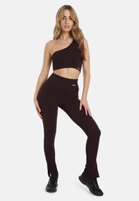 Zwarte geribbelde crop top met één schouder en bijpassende hoge taille leggings met zijsplits en metalen accenten op beide stukken.