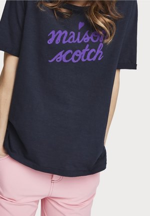 Marineblaues kurzärmeliges Hemd mit lila "maison scotch" Schriftzug und Herz oben, getragen zu hellrosa Hose.