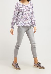 Blusa floral de manga larga en blanco, púrpura y rosa; jeans ajustados gris claro; zapatos gris metálico con cordones y suela plana.