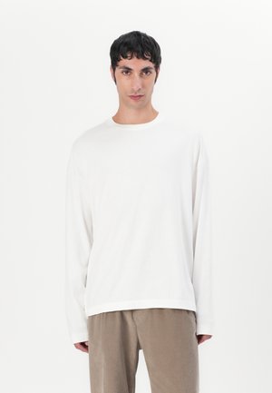 Langærmet hvid T-shirt i blødt stof med runde halsudskæring og afslappet pasform, kombineret med brune kordfløjl bukser. Minimalistisk design.