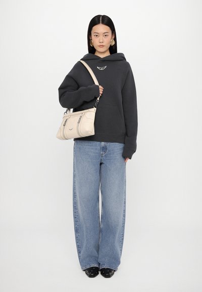 Hoodie noir avec une poche avant, un jean bleu clair ample et un sac à main crème avec des détails en zip et un logo.