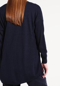 Námorně modrý svetr s dlouhým rukávem a uvolněným střihem, s kulatým lemem a žebrovanými manžetami, vyrobený z měkké pleteniny.