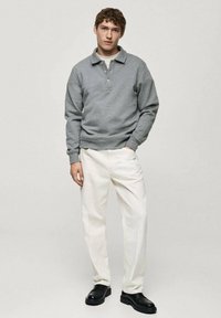 Grå sweatshirt med krage, långa ärmar och elastisk nederdel; kombinerad med gräddfärgade byxor och svarta skor.