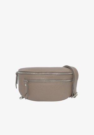 Femme portant un sac bandoulière en cuir taupe sur un haut à manches longues noir et un jean gris foncé, sur un fond uni.