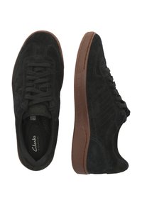 Mustat mokkasneakerit, joissa on teksturoitu päällinen, nauhakiinnitys ja ruskeat kumipohjat. Varustettu brändilogolla ja hienovaraisilla ompeluyksityiskohdilla.