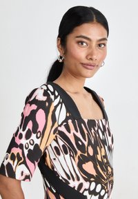 Square-neck dress featuring a butterfly print in pink, black, and cream, accented with solid black shoulders and a smooth texture.