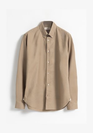 Camisa de manga larga de algodón beige. Presenta un cuello clásico, botones blancos y un dobladillo curvado con aberturas laterales para facilitar el movimiento.