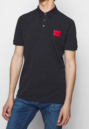 Černé polo tričko vyrobené z bavlny, s červenou obdélníkovou nášivkou se znakem "HUGO", tříknoflíkovým zapínáním a krátkými rukávy.