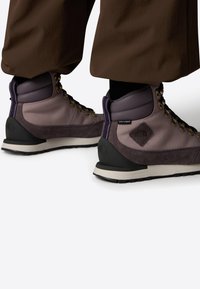 Botas de senderismo en tonos púrpura y gris, fabricadas con materiales de ante y tejido, que cuentan con ojales de metal, un collar acolchado y una suela texturizada.