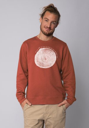 Rostfarbenes Sweatshirt mit Rundhalsausschnitt, das ein weißes Baumring-Grafikdesign und Text darum herum zeigt. Weicher Stoff mit lockerer Passform.