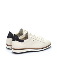 Zapatillas de cuero blanco con un acento negro en el talón, superficie texturizada, punta redonda, cierre de cordones y una suela de goma en contraste.