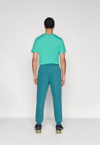 Τυρκουάζ κοντομάνικο μπλουζάκι και πράσινο-μπλε αθλητικό παντελόνι με ελαστική μέση. Το παντελόνι στενεύει στους αστραγάλους και συνδυάζεται με μαύρα αθλητικά παπούτσια.