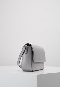 Šedá kožená kabelka obdélníkového tvaru, hladkého povrchu a s klopou. Obsahuje ramenní popruh a minimalistické stříbrné kovové prvky.