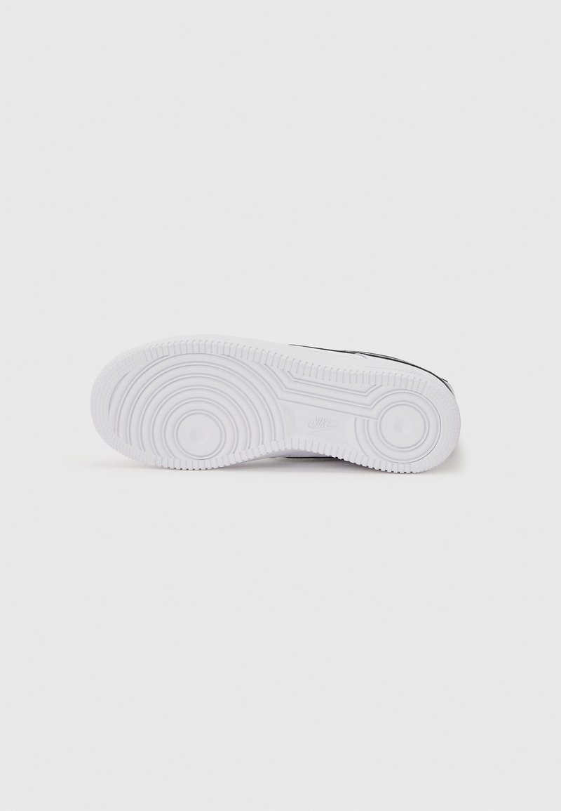 Semelle blanche de chaussure Nike avec des motifs de rainures circulaires et un logo Nike en relief sur un fond uni gris clair.