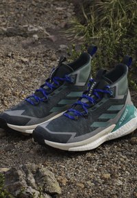 Schwarze und grüne Sportschuhe mit einer strukturierten Oberseite, blauen Schnürsenkeln und einer weißen Sohle, die ein markantes "TERREX"-Logo zeigt.