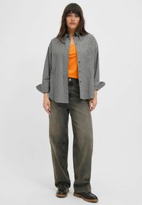 Crno-bijela gingham oversized košulja, narančasta majica ispod, sivi široki traperice i crne čipkaste cipele s debelim potplatima.
