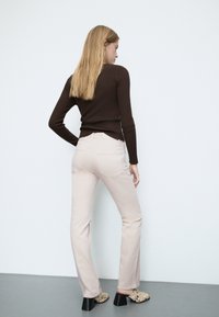 Jasnoróżowe, dopasowane dżinsy z lekkim rozszerzeniem, z tylnymi kieszeniami i wysokim stanem. Połączone z ciemnoczekoladowym, ryżowym topem oraz wzorzystym obuwiem.