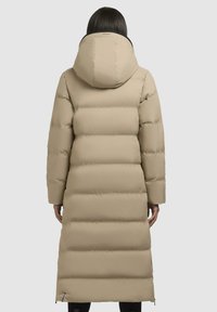 Beige gewatteerde jas met een capuchon, met een lange snit, horizontale stiksels en zijritsen. Glad, mat textiel met minimale accenten.