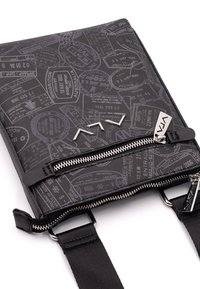 Borsa a tracolla nera con tessuto strutturato decorato con timbri da viaggio in rilievo, hardware argentato, due scomparti con cerniera e spallacci regolabili.