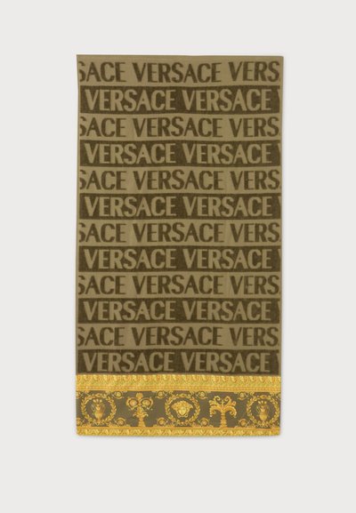 Καφέ ύφασμα με επαναλαμβανόμενο κείμενο «"VERSACE"» σε σκούρο καφέ και χρυσό διακοσμητικό περίγραμμα με κλασικά μοτίβα στο κάτω μέρος.