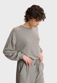 Pullover grigio a maniche lunghe realizzato in tessuto morbido, con scollatura rotonda e vestibilità rilassata. Abbinato a pantaloni jogger con vita regolabile in tinta.