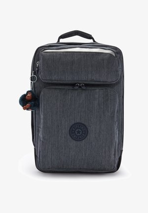 Grijze stoffen rugzak met meerdere ritscompartimenten, een ronde logopatch en een harige aap sleutelhanger eraan bevestigd.