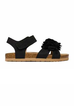 Schwarze Sandale mit Korksohle, verstellbarem Knöchelriemen und großem Stoffblumendetail über den vorderen Riemen.