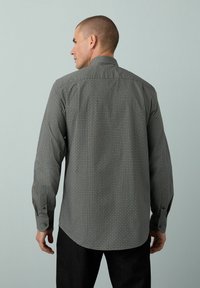 Grå mønstret langærmet skjorte med ståkrave, knapmanchetter og et geometrisk print på et struktureret stof, set fra ryggen.