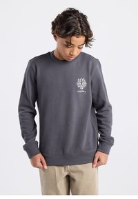 Grey crewneck sweatshirt made of cotton blend with ribbed cuffs. Features a white graphic logo on the left chest. Smooth texture.