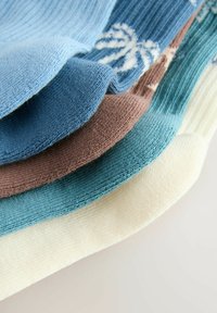 Pila de calcetines de punto doblados en colores azul claro, azul oscuro con patrón blanco, marrón, verde azulado y crema sobre una superficie clara.