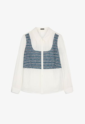 Camicia bianca a maniche lunghe con un pannello in tweed blu sul petto, colletto e chiusura con bottoni. Dettaglio del tessuto testurizzato visibile.