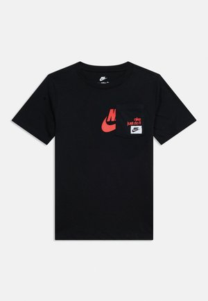 T-shirt noir à manches courtes Nike avec un swoosh rouge, un texte rouge « nike just do it » et une poche noire avec logo Nike blanc sur le côté avant gauche.