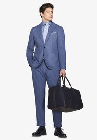 Completo azzurro a righe con camicia e cravatta coordinate, abbinato a una borsa a tracolla blu scuro con dettagli marroni e scarpe nere.